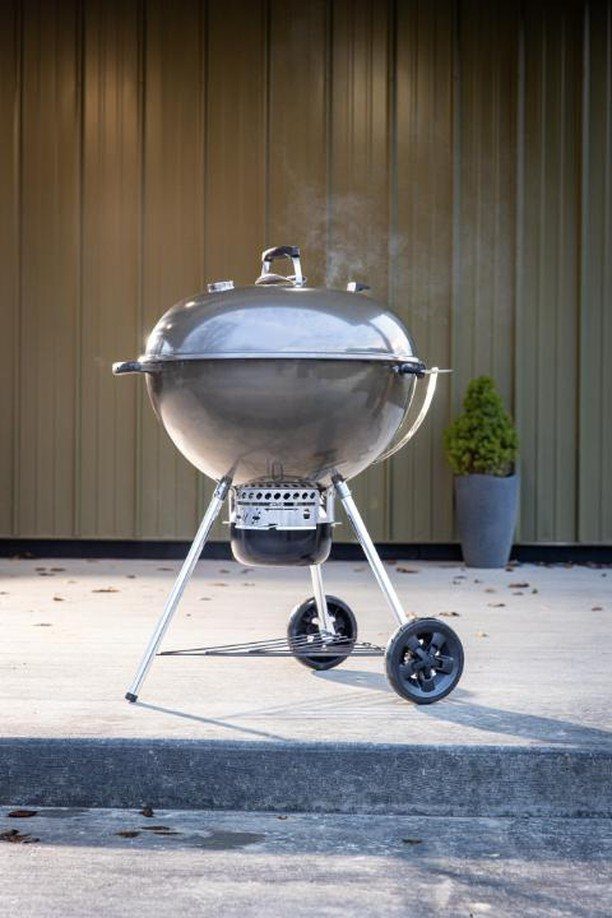 Silver charcoal grill on a concrete patio against a brown slatted wall.
