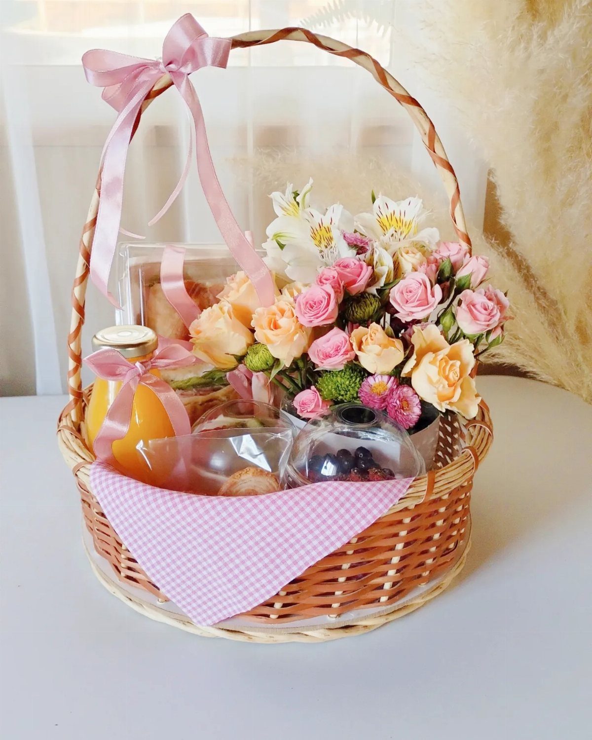Wicker gift basket with orange juice, pink roses, and pastries for breakfast.