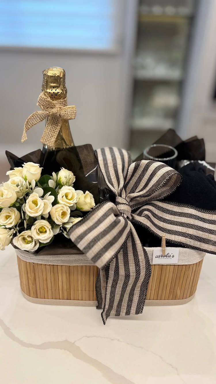 Gift basket with white roses, champagne, and a large striped ribbon on marble.