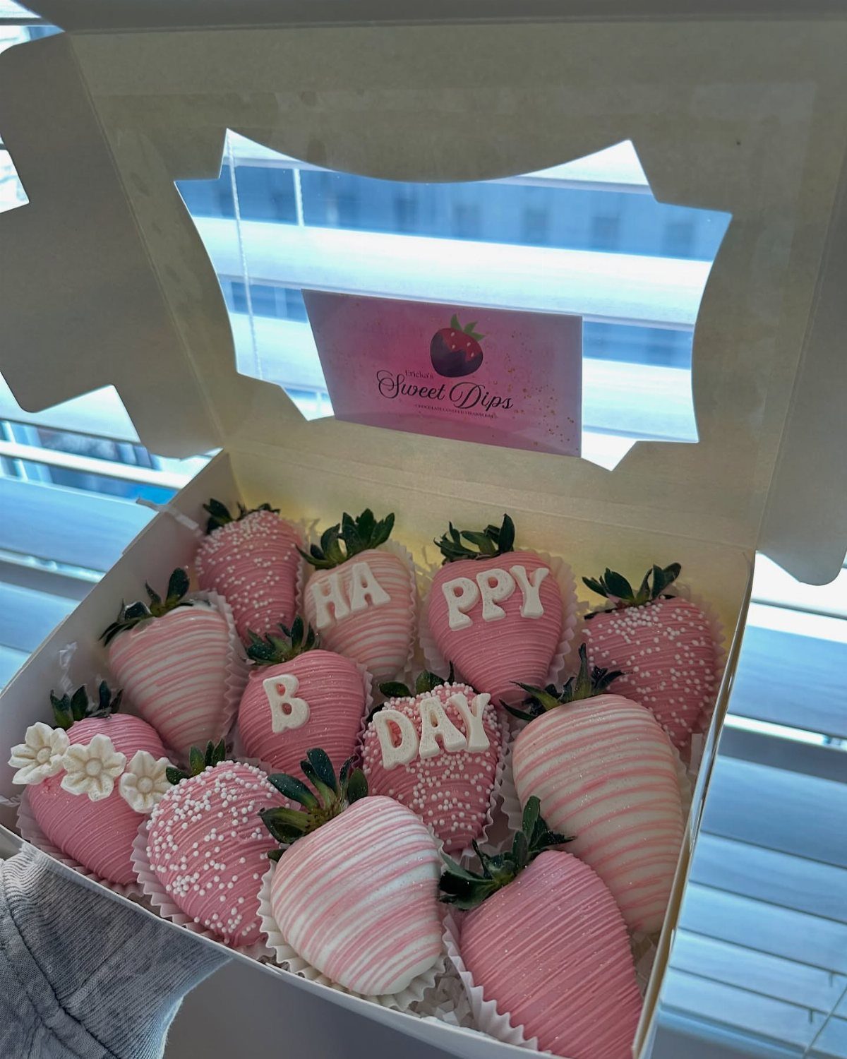 Pink chocolate-covered strawberries in a white box, some decorated with birthday lettering.