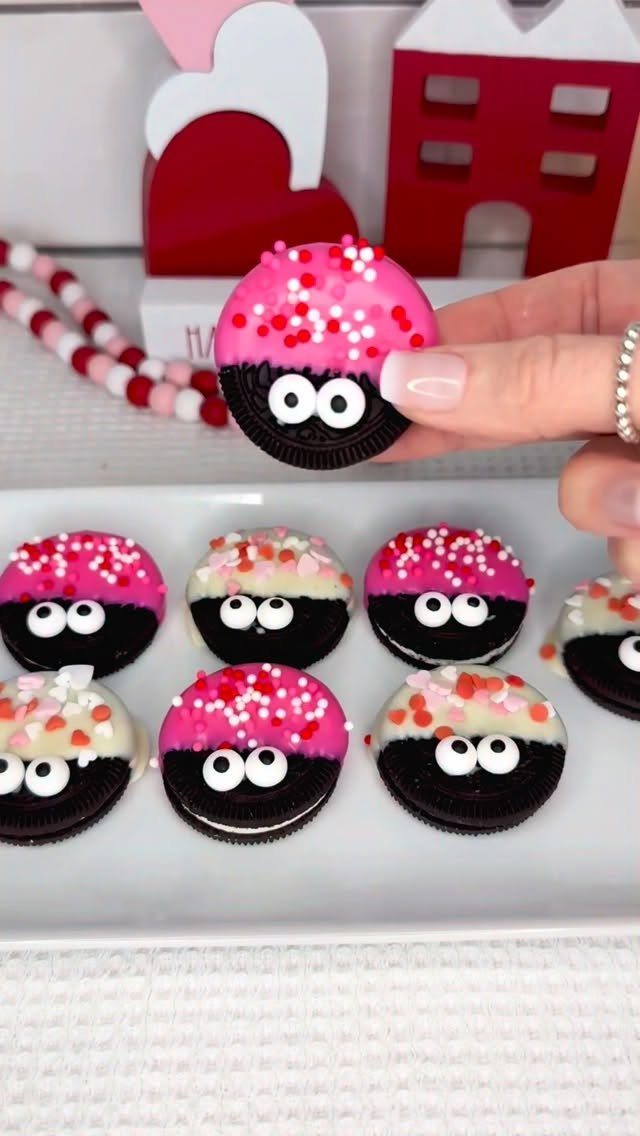 Decorated chocolate sandwich cookies with pink frosting and candy eyes on a plate