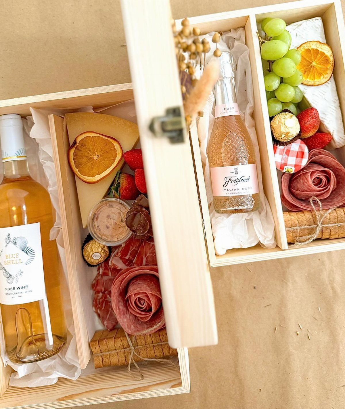 Two wooden gift boxes filled with rosé wine, cheese, salami roses, and fruit.
