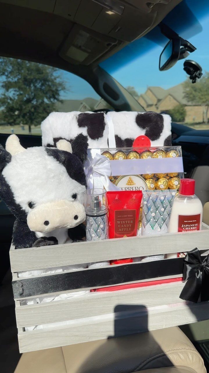 Gift crate with plush cow, chocolates, and toiletries sitting on a car seat.