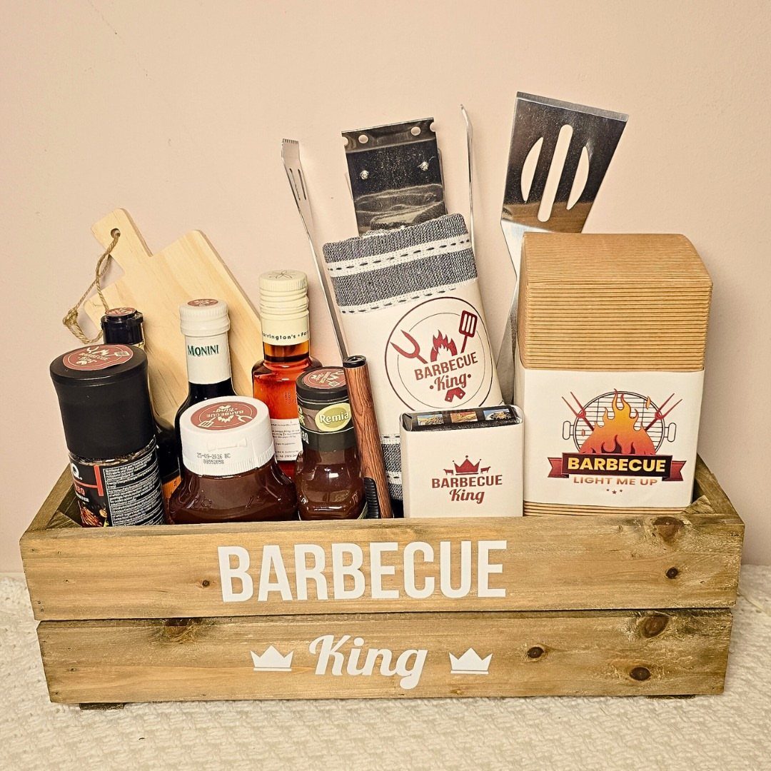 Wooden barbecue gift crate filled with sauces, spices, and metal grilling tools.