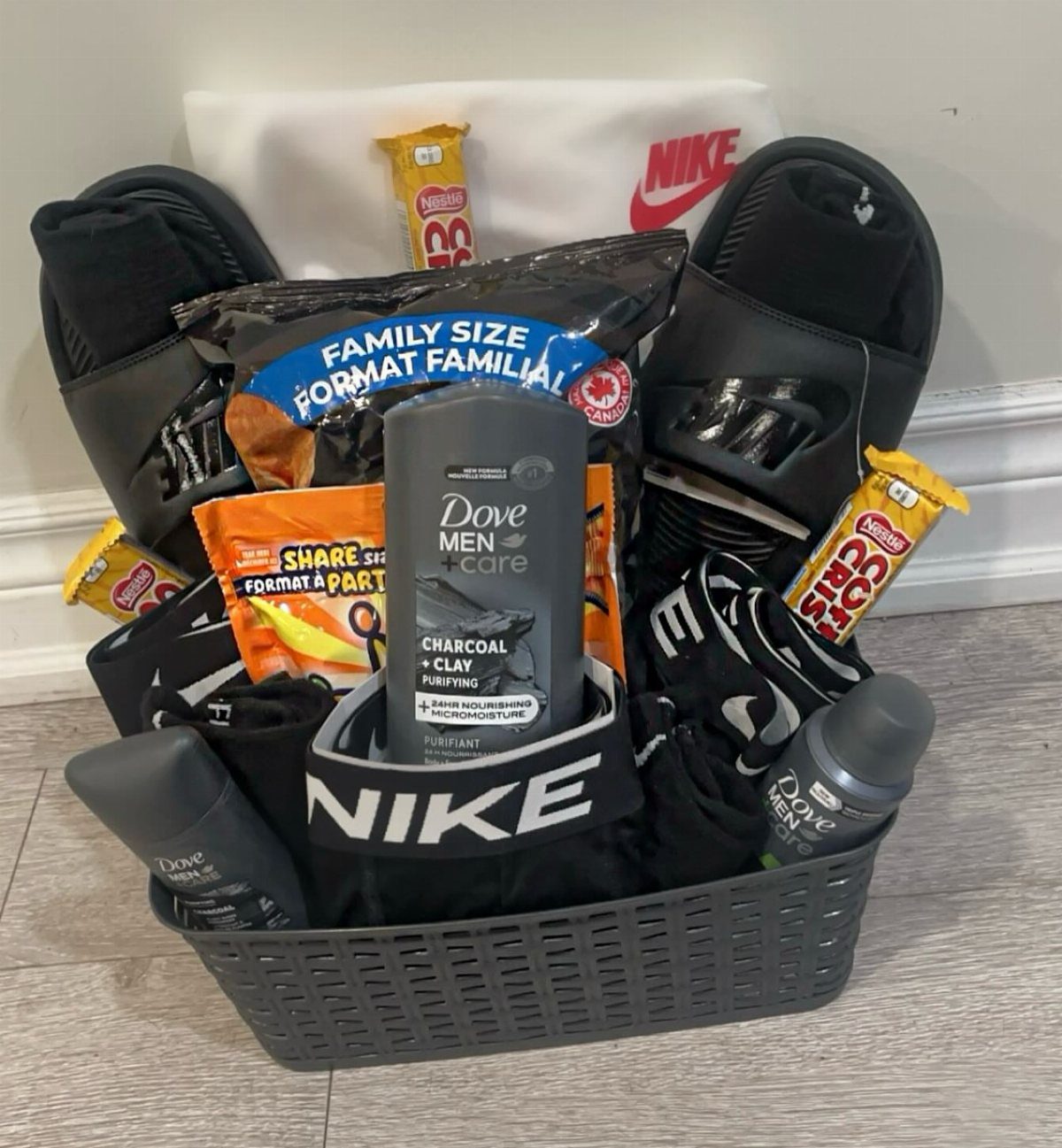 Grey gift basket filled with Nike apparel, Dove men's care, and assorted snacks.