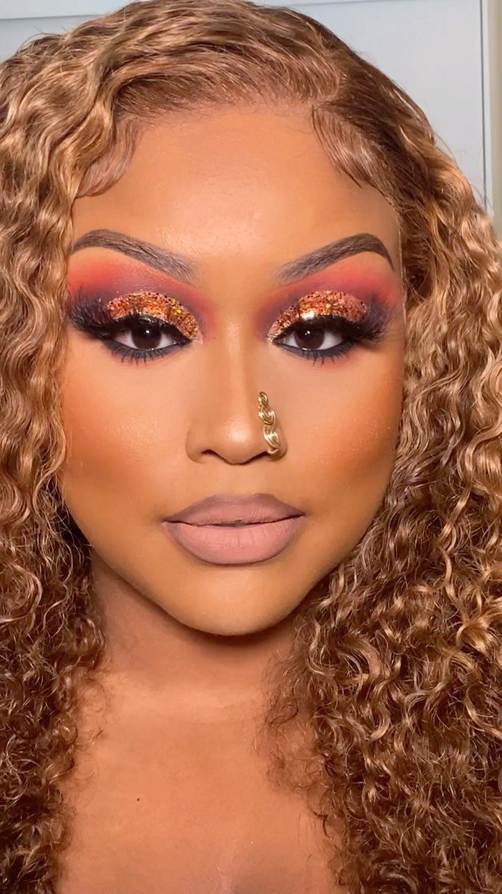 Woman with curly blonde hair wearing burnt-orange glitter eyeshadow and nude lipstick.