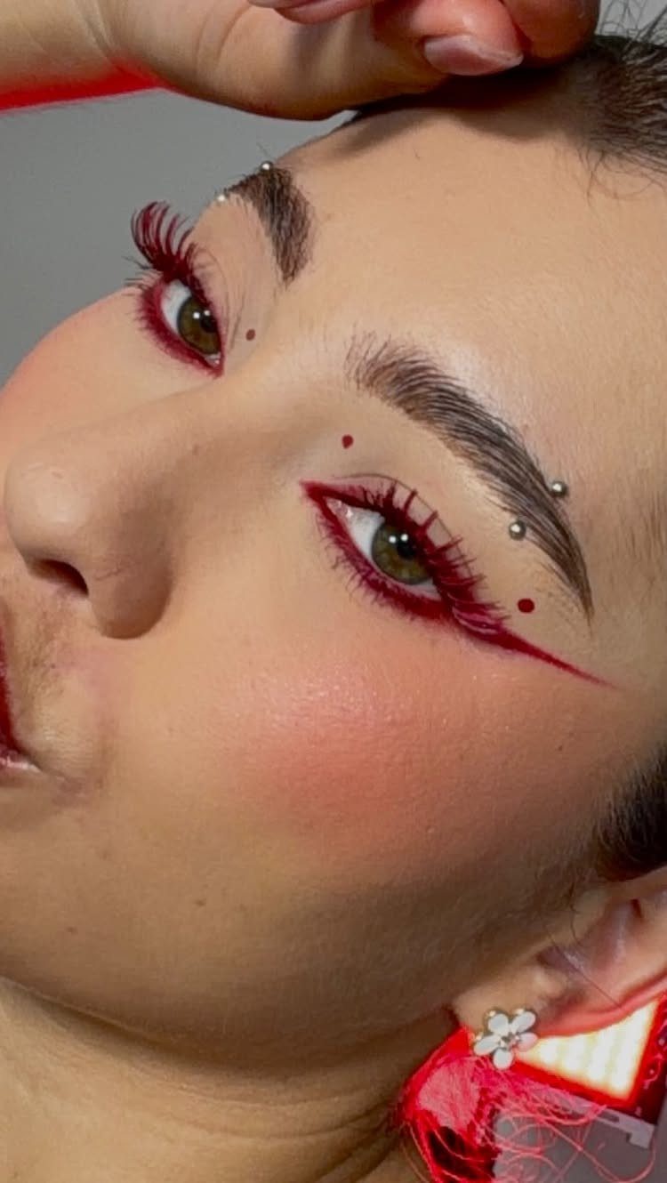 Person with bold red winged eyeliner, red facial accents, and red cheek blush.