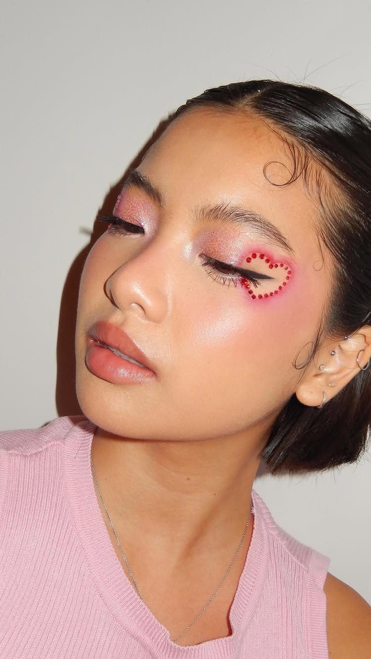 Woman with pink eyeshadow and a red glitter heart on her cheek.