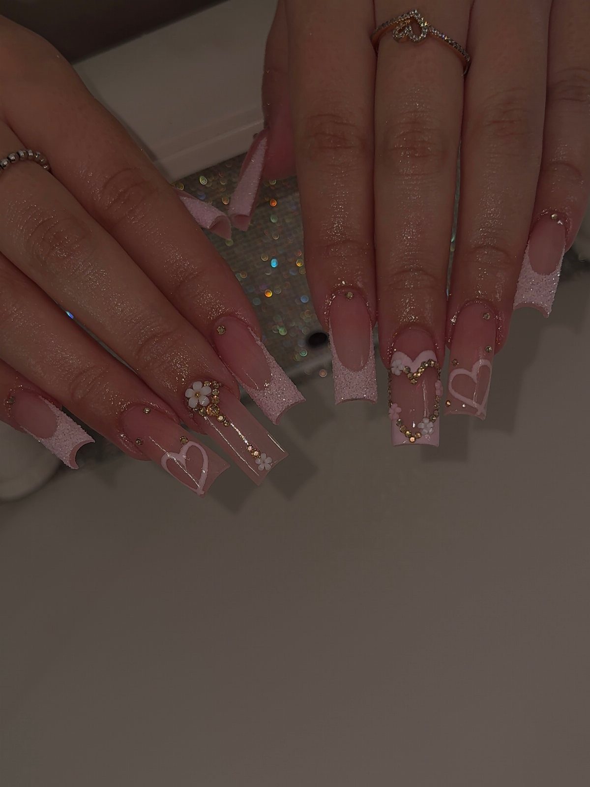 Square acrylic nails with pink French tips, white hearts, and floral nail art.