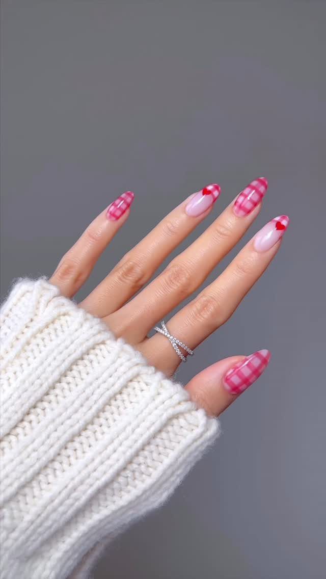 Square nails with pink gingham patterns and red hearts on a manicured hand.