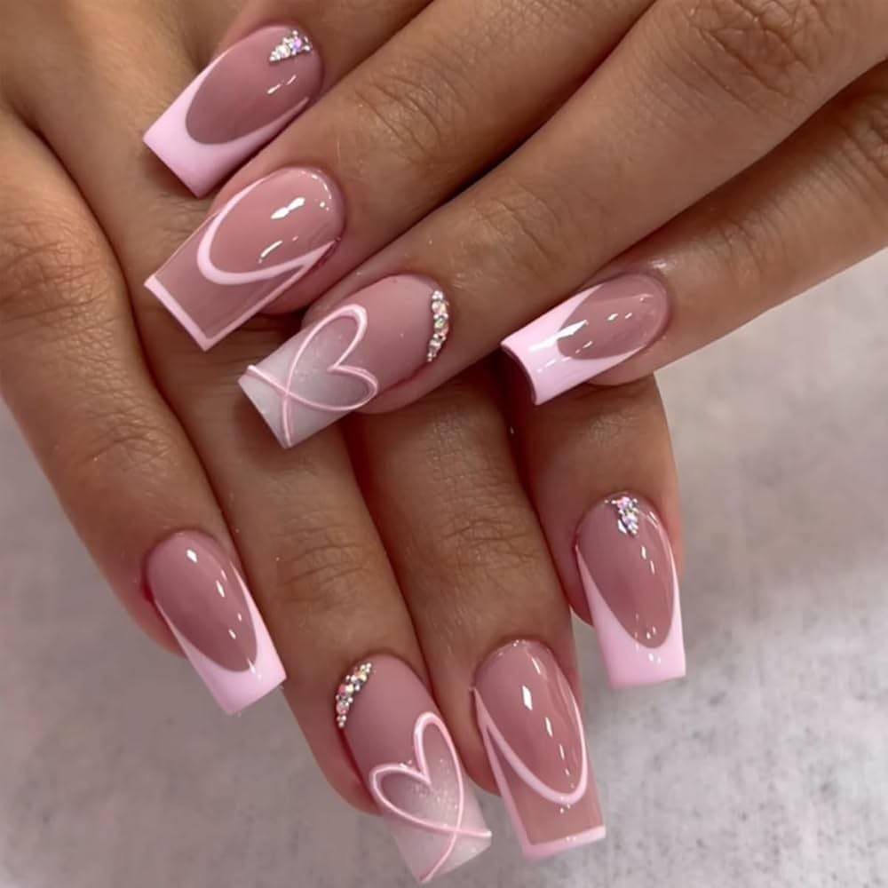 Square acrylic nails with nude base, pink tips, white hearts, and rhinestones.