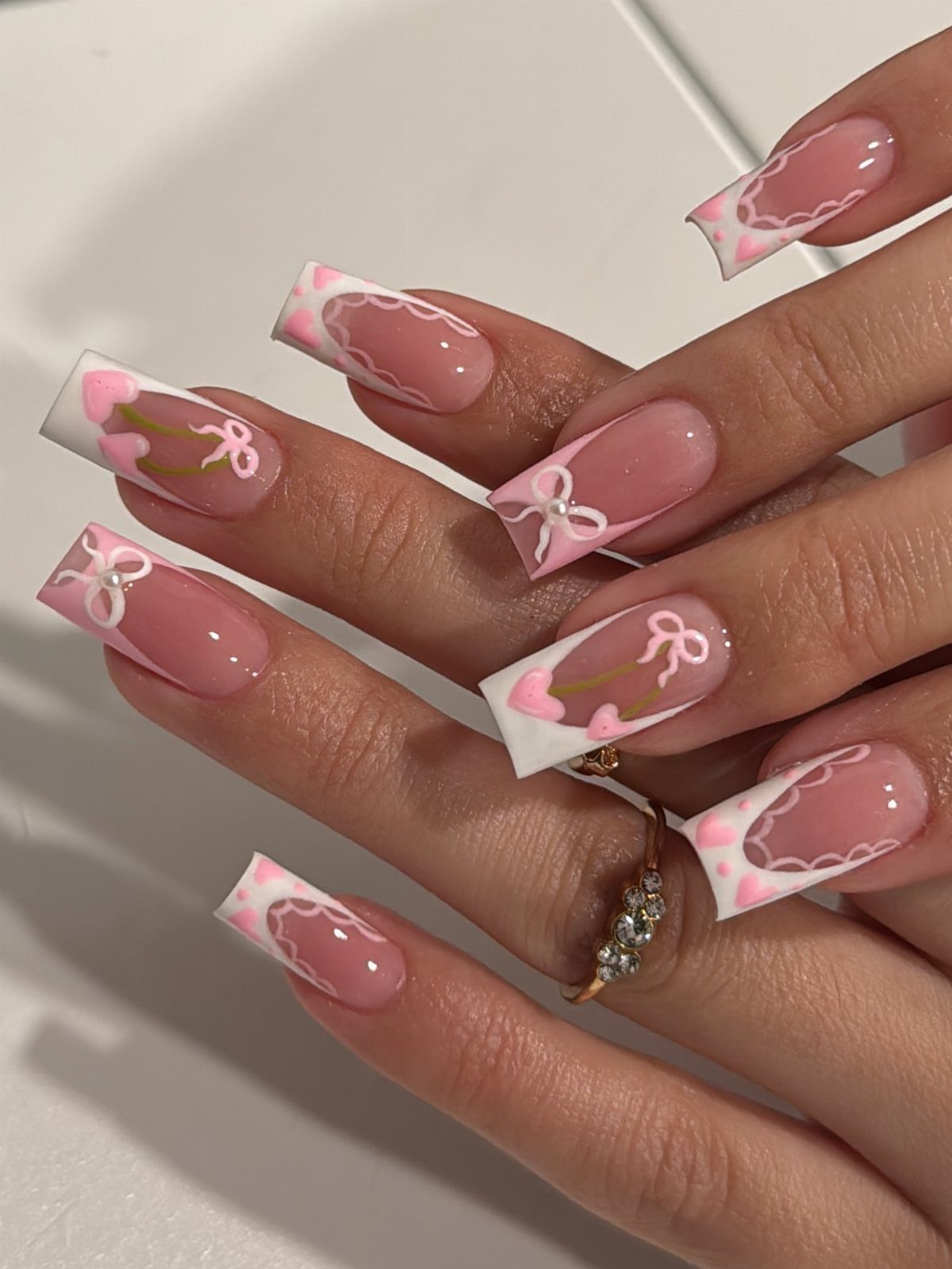 Square acrylic nails with pink hearts and white bows for Valentine's Day.