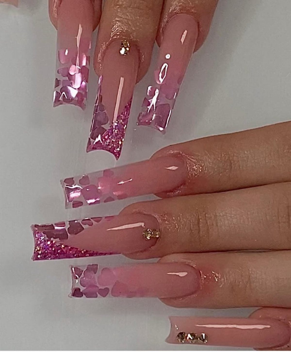 Long square pink nails featuring glitter, heart sequins, and small sparkling rhinestones.