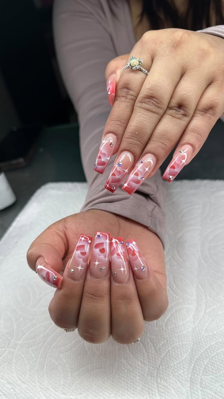 Square acrylic nails with red and white heart designs and small sparkling rhinestones.
