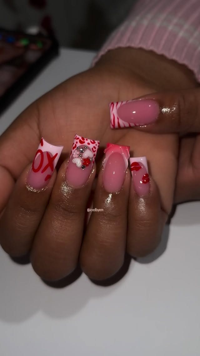 Square acrylic nails with pink and white polish, red hearts, and XOXO lettering.