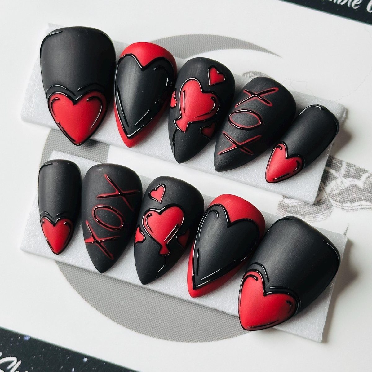 Matte black stiletto nails decorated with red hearts and XOXO lettering