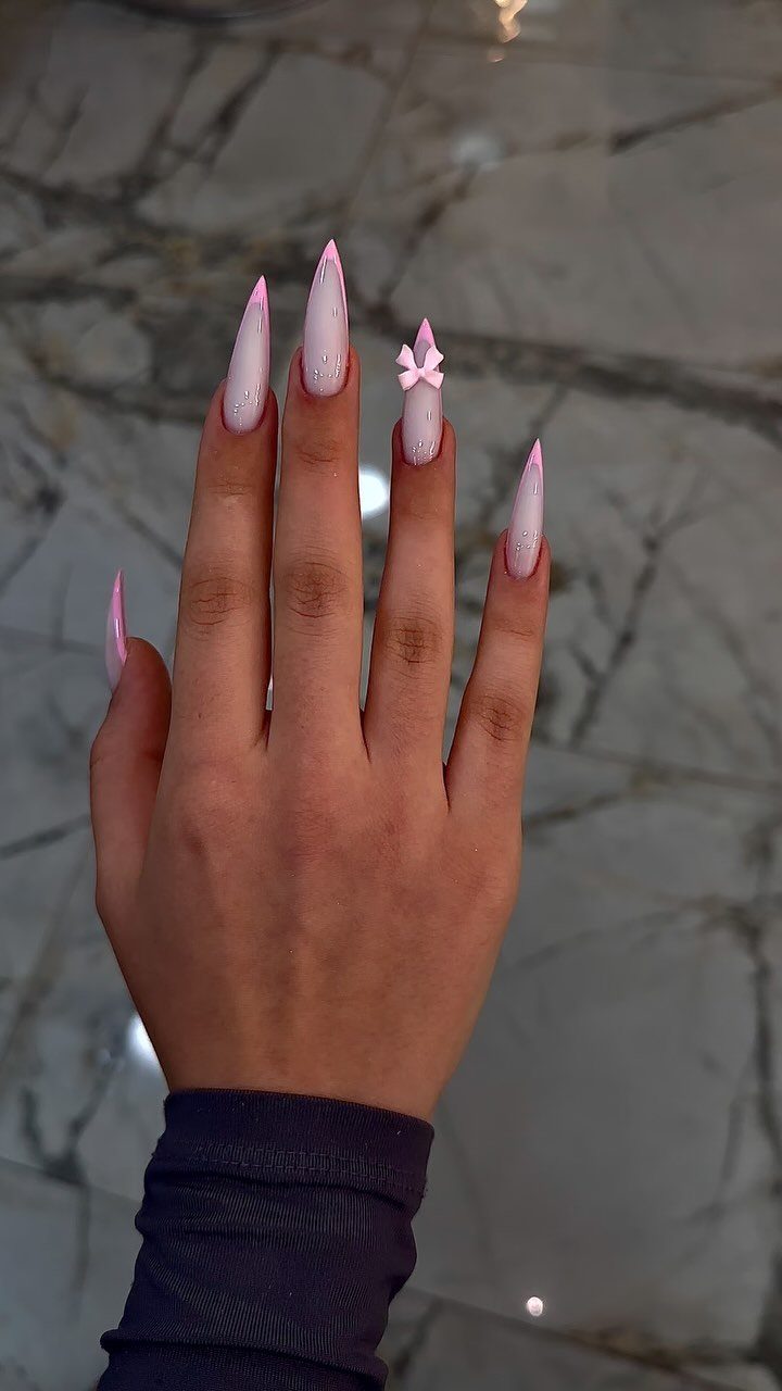 Nude stiletto nails with pink tips and a small pink 3D bow decoration.