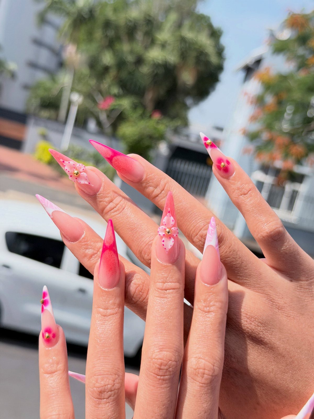 Stiletto acrylic nails with pink and white ombre and small 3D floral accents.