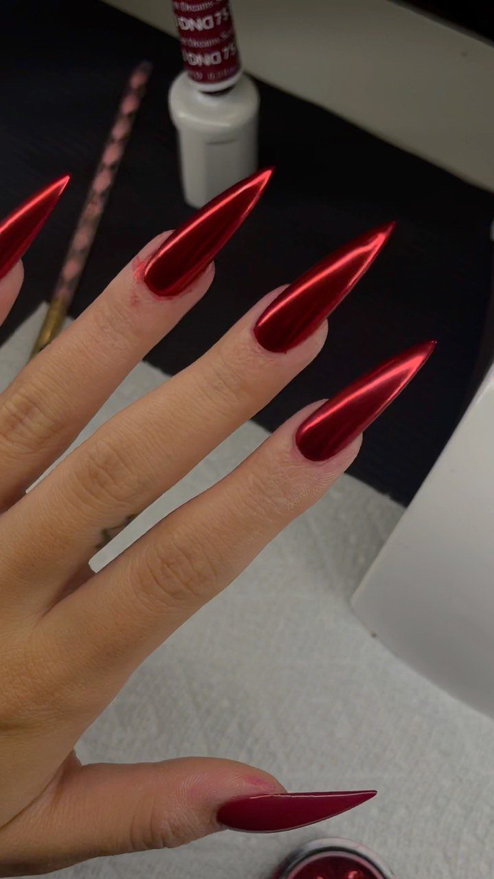 Long stiletto nails with a metallic red chrome finish on a hand.