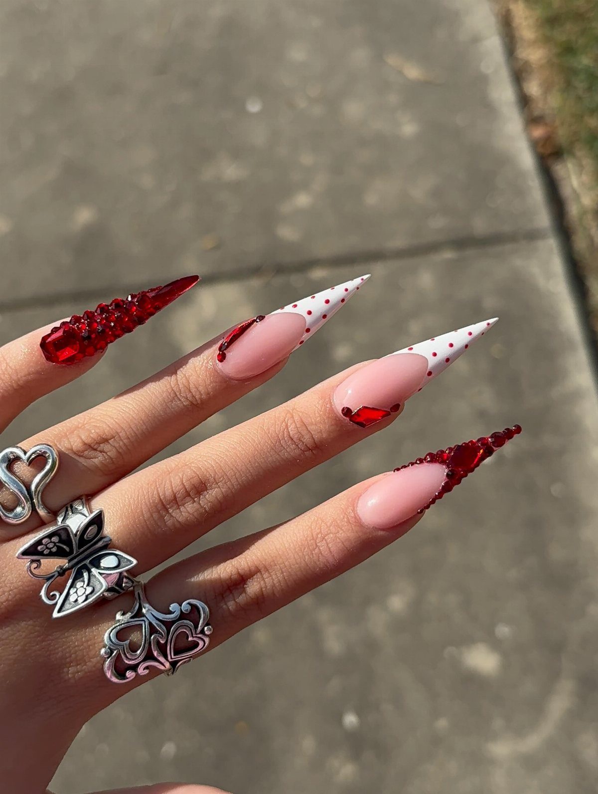Stiletto nails with red and nude polish, red polka dots, and red crystals.