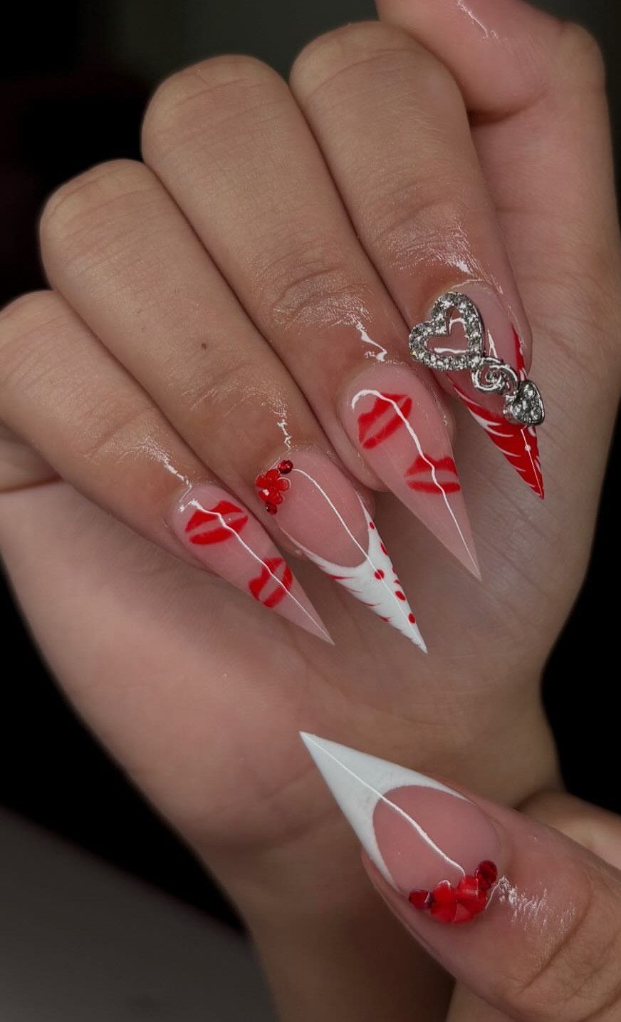 Stiletto nails with nude base, red lip art, and silver heart charm.