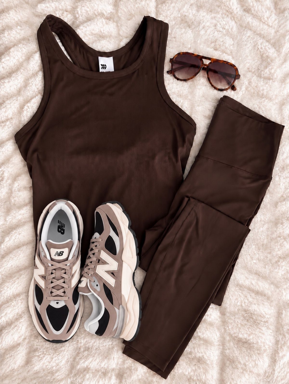 Brown athletic tank top and leggings with beige sneakers and sunglasses on white fabric.
