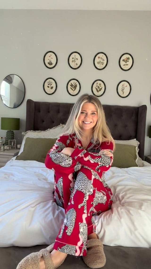 Woman in red patterned Christmas pyjamas and fluffy slippers sitting on a bed.