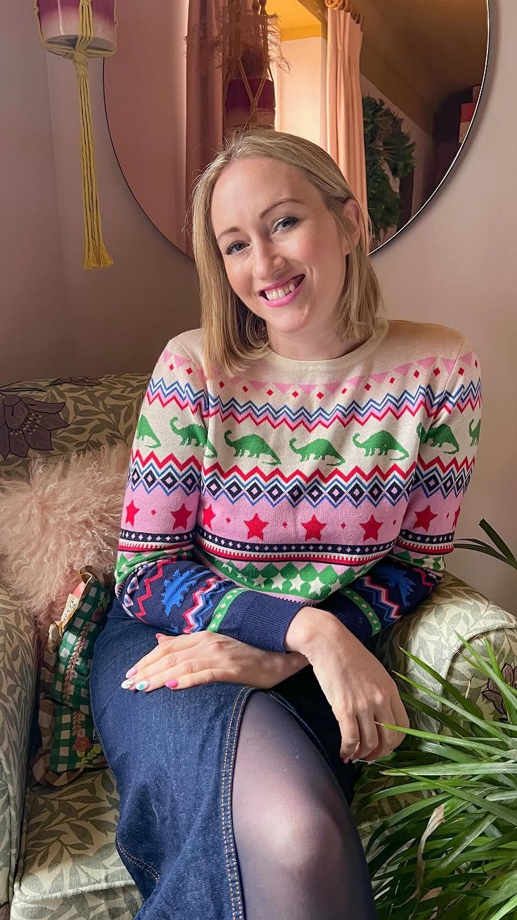 Woman wearing a colorful Fair Isle sweater with dinosaurs and a denim skirt.