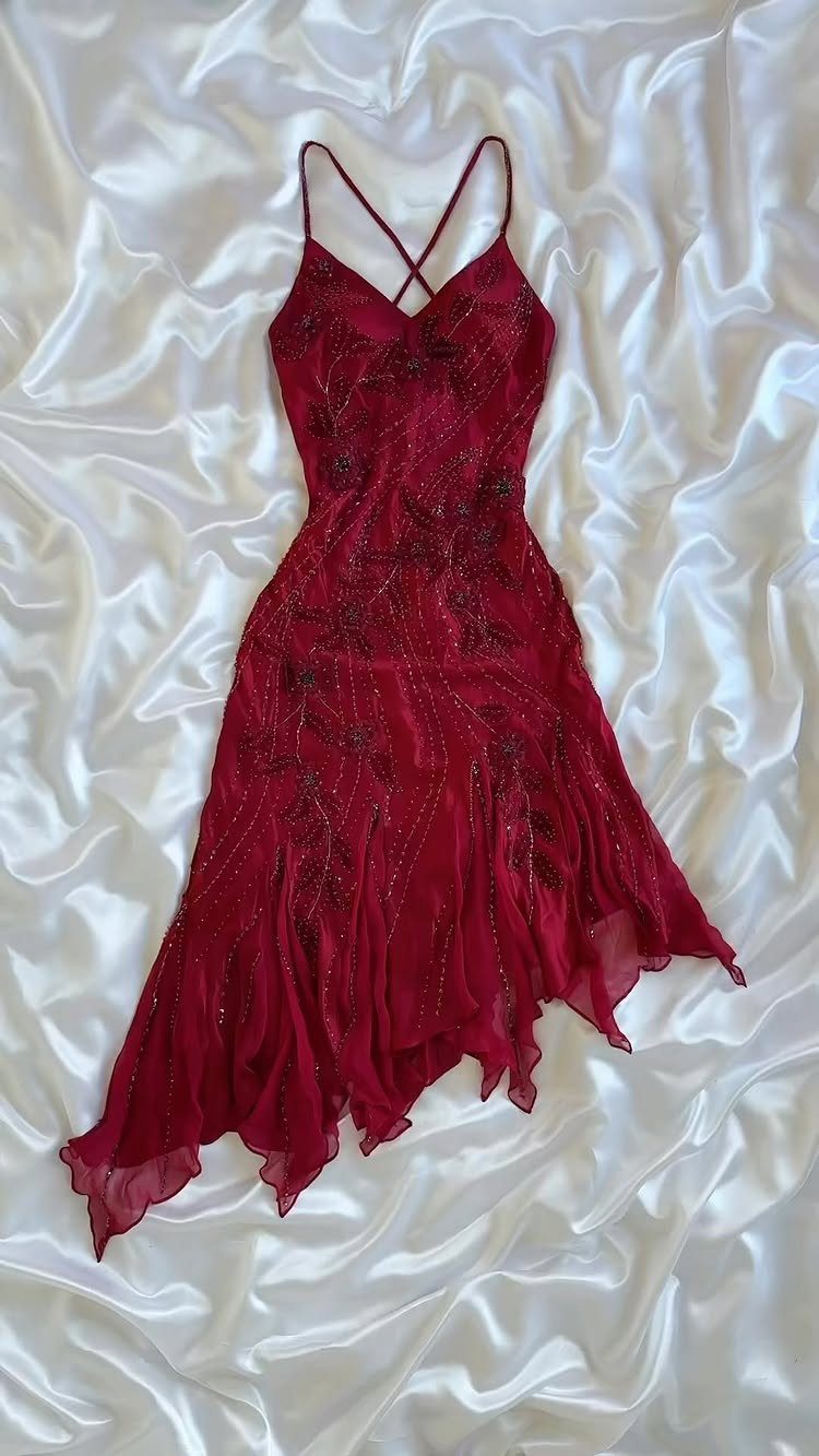 Red sequined dress with thin straps resting on white satin fabric.