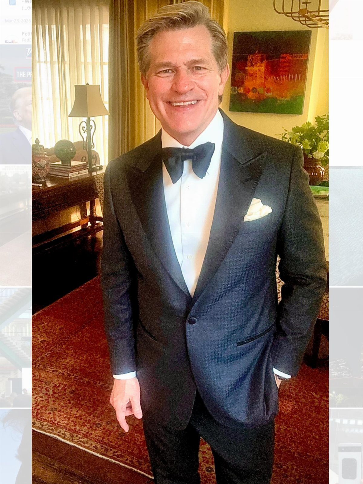 Man in a black tuxedo with a bow tie smiling in a room.