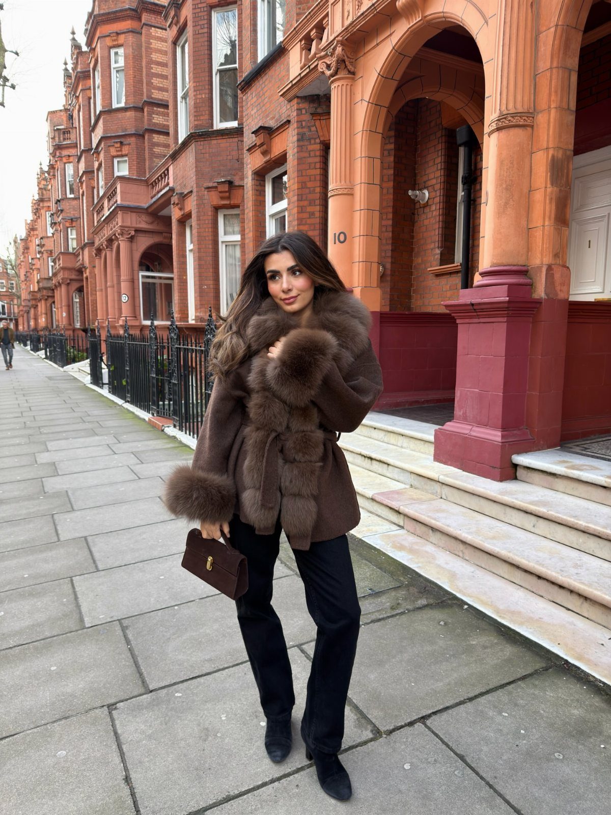 Woman wearing a brown faux-fur coat and black trousers on a city street