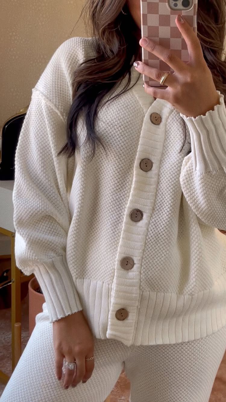 Woman wearing a cream-colored matching knit cardigan and trouser set in a mirror selfie.
