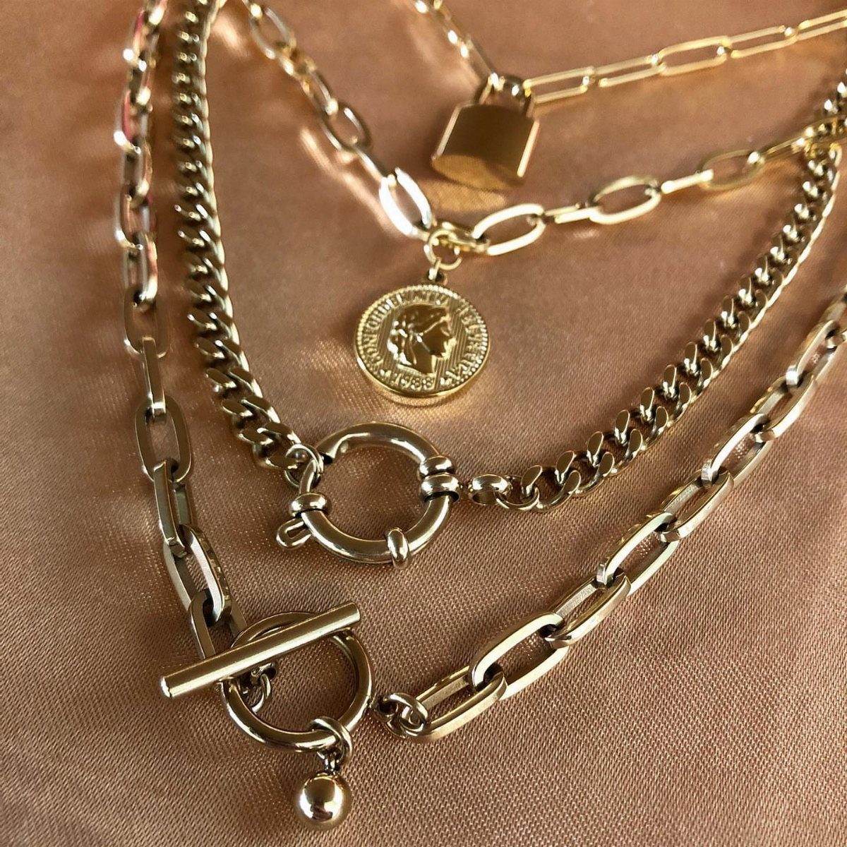 Gold chunky chain necklaces with a coin pendant on shimmering gold fabric