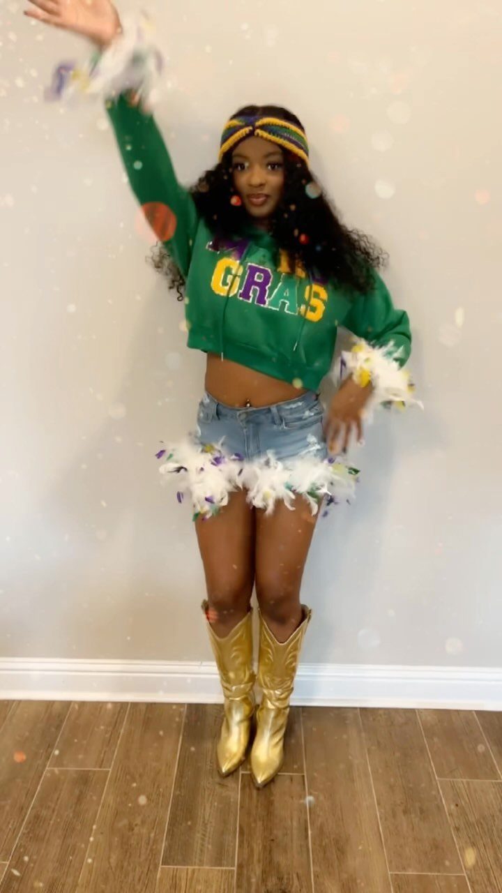 Woman in green Mardi Gras sweatshirt, feathered denim shorts, and gold cowboy boots.