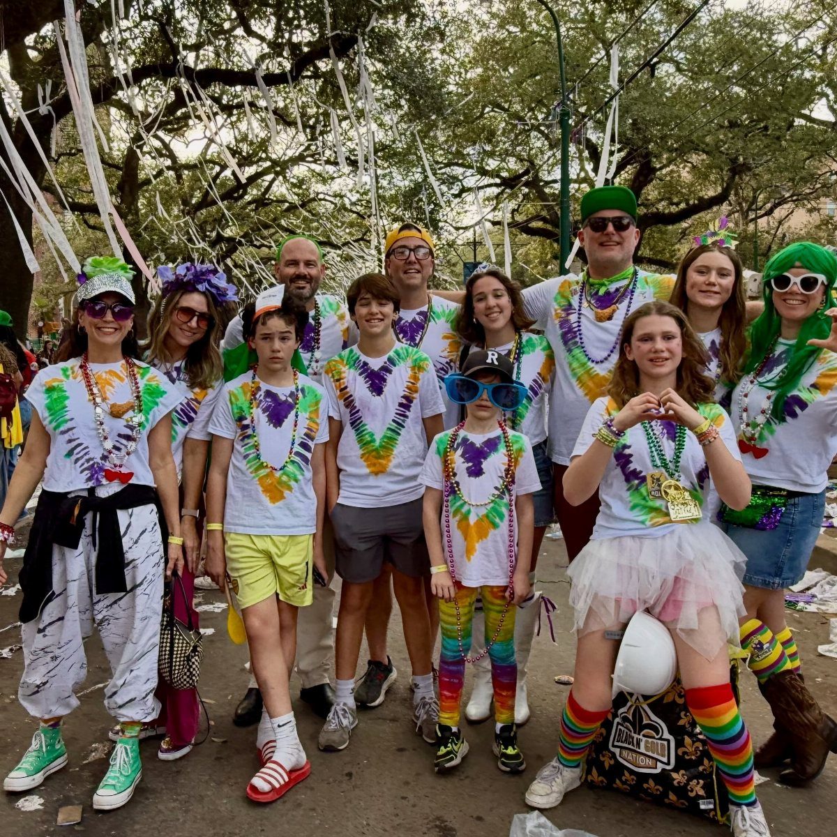 Group of people wearing white shirts and purple, green, and gold Mardi Gras beads.
