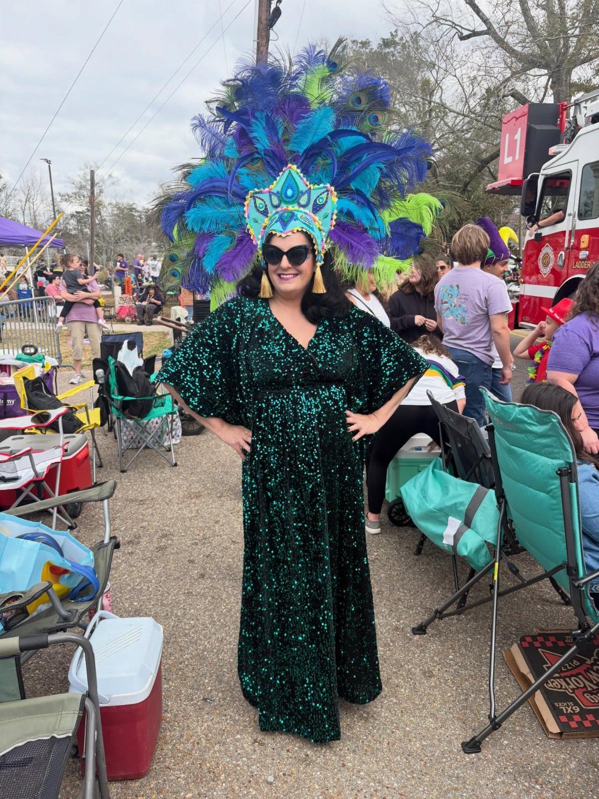 Woman in a green sequined dress and large colorful feathered Mardi Gras headdress.