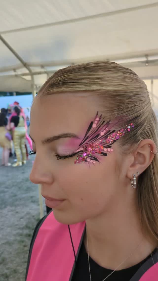 Woman with pink glitter and gems applied around her eye and temple.