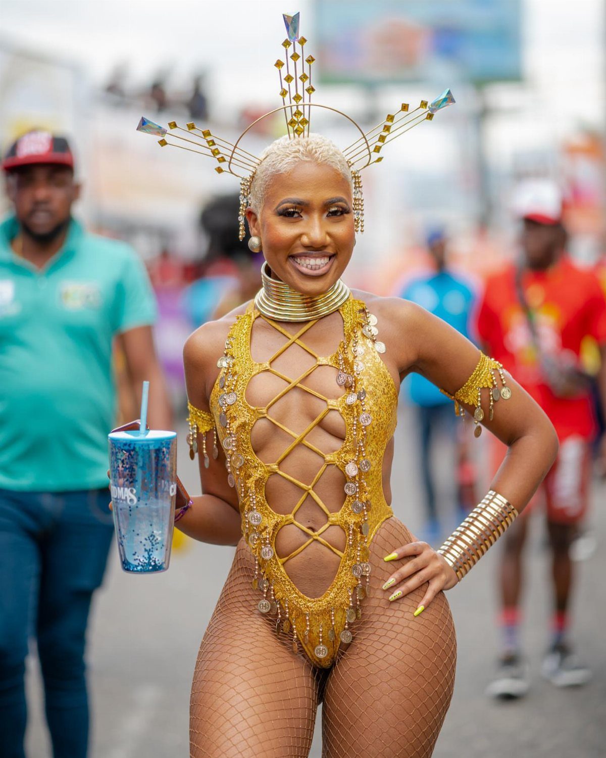 Woman in an elaborate gold sequined bodysuit and headpiece smiling at a parade.