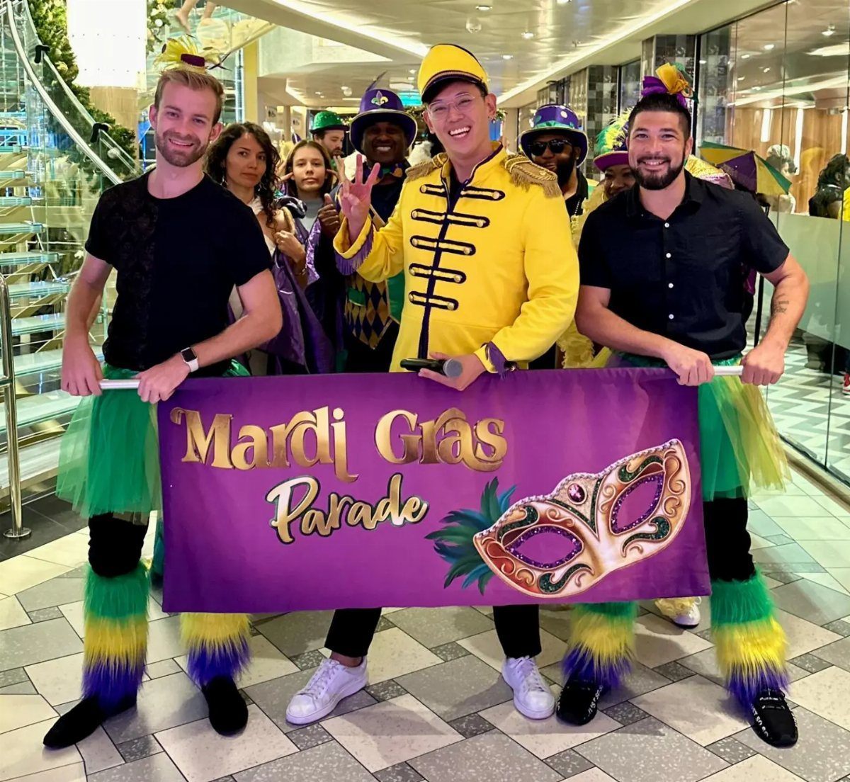 Group of people in colorful Mardi Gras costumes holding a purple parade banner.
