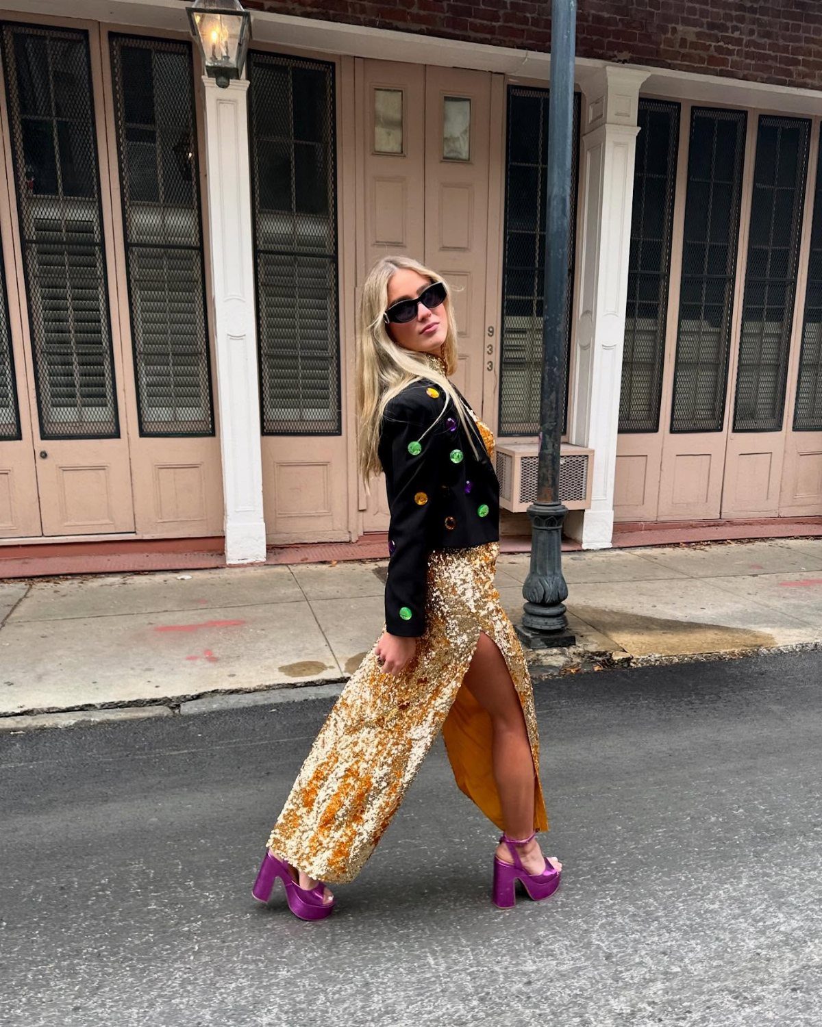 Woman in gold sequined skirt, black jacket, and purple platform heels on city street