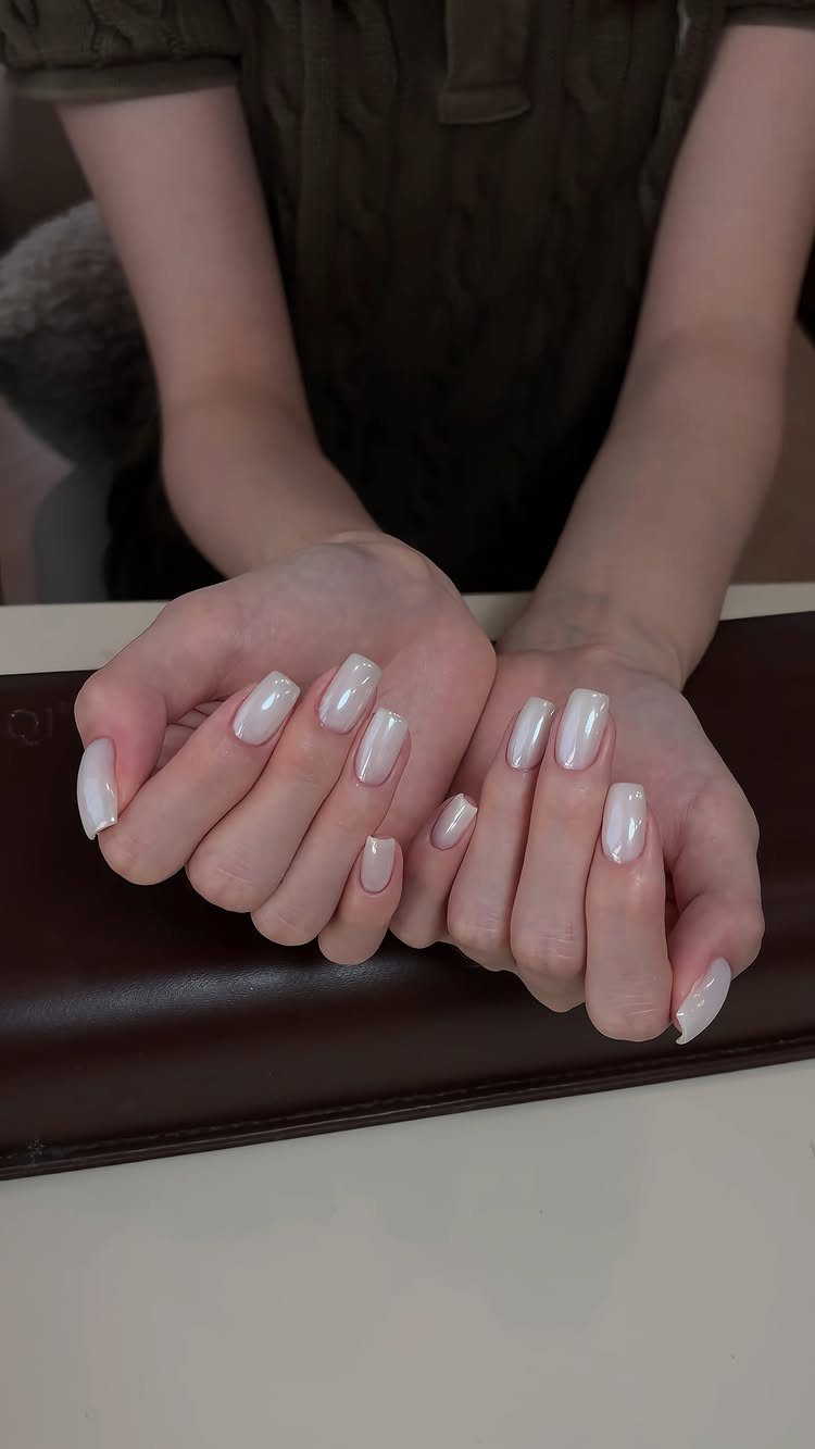 Hands with long almond-shaped nails painted in a shimmering chrome white polish.