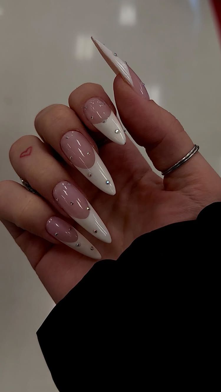 Stiletto nails with white French tips and small silver rhinestones on a hand.