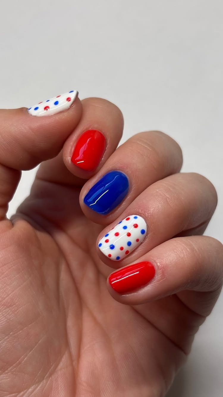 Hand with red, blue, and white polka dot patriotic nail polish design.