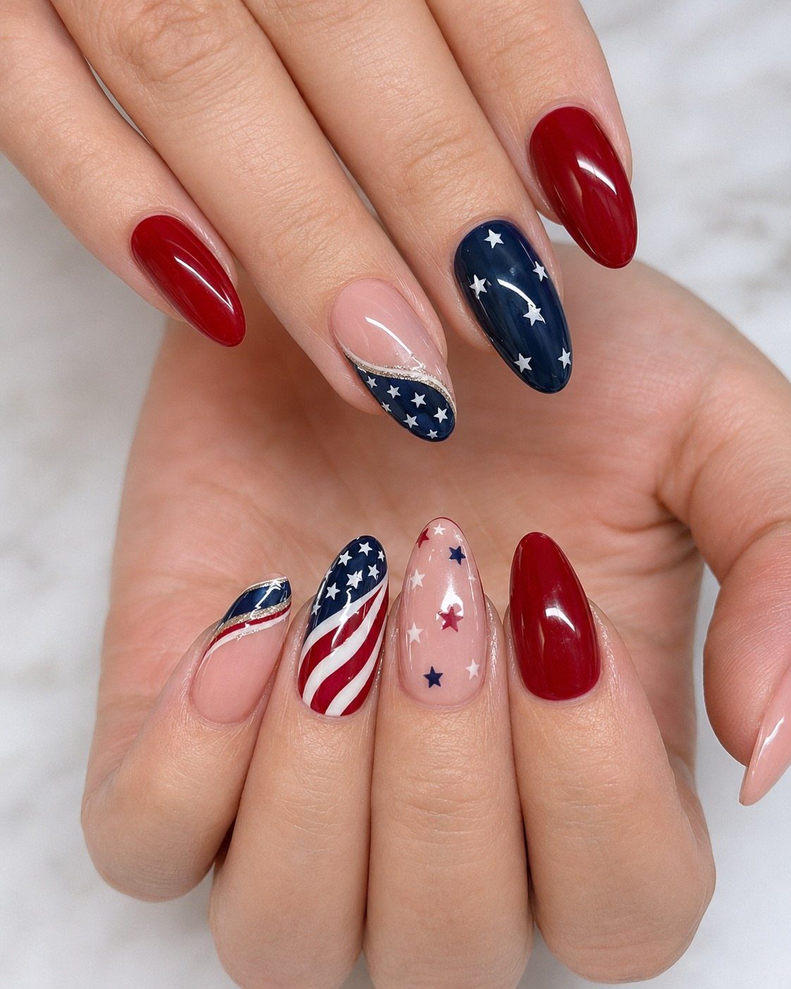 Almond-shaped nails with red, white, and blue patriotic designs including stars and stripes.